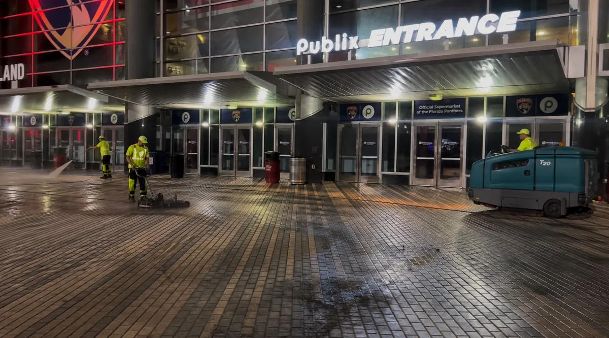 Crew pressure cleaning and sweeping a stadium entrance plaza at night