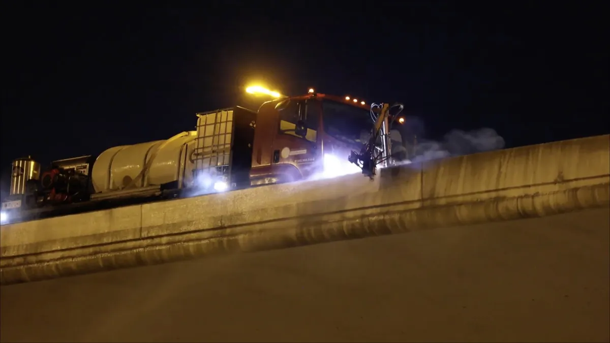Highway wall cleaning truck washing a concrete roadway wall at night