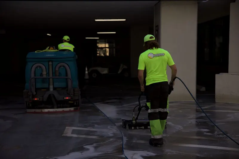 Crew member using a surface cleaner attachment on a parking garage deck
